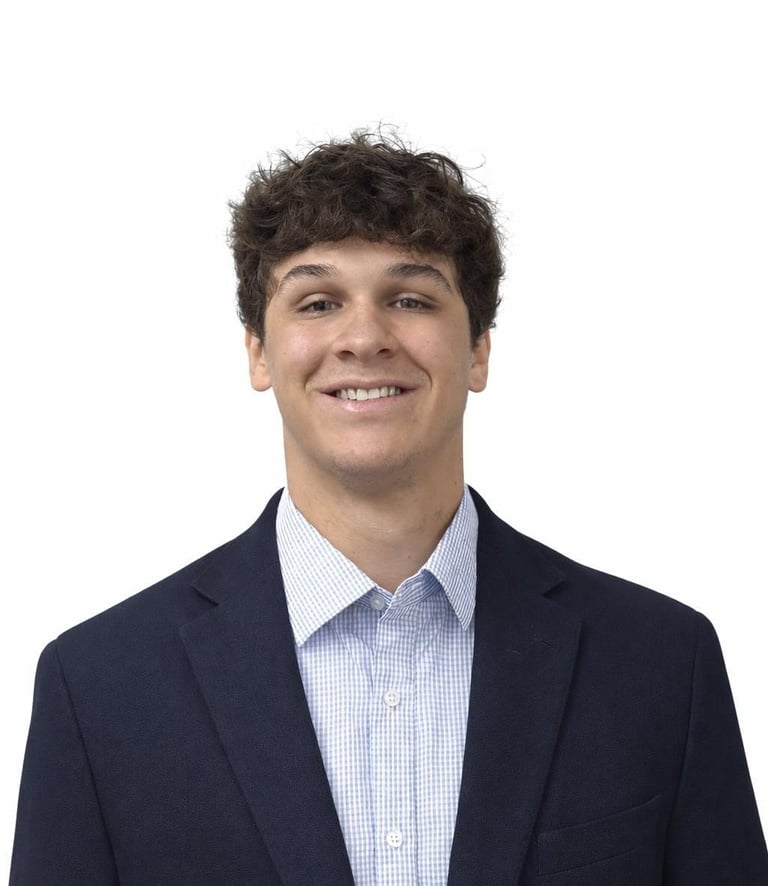 Smiling man with dark curly hair wearing a dark navy blazer and light blue checkered dress shirt